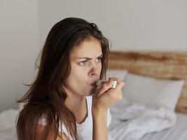 mujer participación un termómetro en su boca mientras sentado en el cama temperatura salud problemas foto