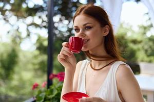 retrato de joven hermosa mujer con rojo taza de café al aire libre café verano día foto