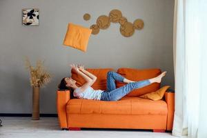 alegre mujer en el naranja sofá en el descanso habitación posando estilo de vida foto