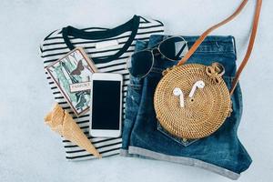 Flat lay, summer women's clothing and accessories. Striped t-shirt, blue shorts, rattan bag, phone photo