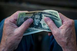 Elderly man holding US dollar bills in hands, 20 dollar note in pensioner's hand photo