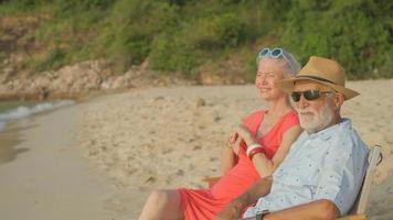 A couple of elderly sitting in chairs at the beach watching the sun and the sea on their summer vacation and they smile and enjoy their vacation. photo