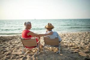 A couple of elderly sitting in chairs at the beach watching the sun and the sea on their summer vacation and they smile and enjoy their vacation. photo