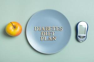 Diabetes Diet Plan text. Glucometer and plate with apple on colored background flat lay, top view photo