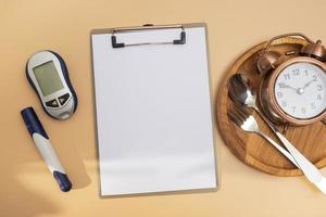 Empty text board and glucometer and cutlery with alarm clock on plate flat lay, top view. Mock up diabetes theme photo