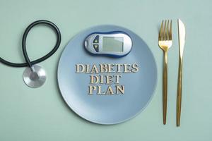 Diabetes Diet Plan text. Stethoscope, glucometer and plate with cuttleries colored background photo