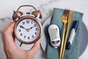 alarma reloj en hembra mano y glucómetro con cuchillería en lámina. diabetes dieta concepto foto