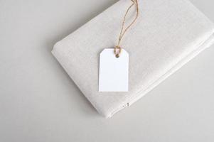 Empty price tag on white fabric, label mockup, folded fabric with tag on white background photo