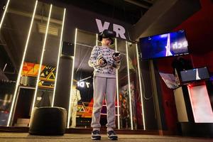 Boy kid playing game using virtual reality headset and gamepads in playing club. photo