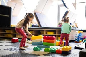 Two sisters playing at kids play center while build with colored plastic blocks. photo