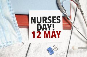 Stethoscope and white card with nurses day 12 may text on notebook photo