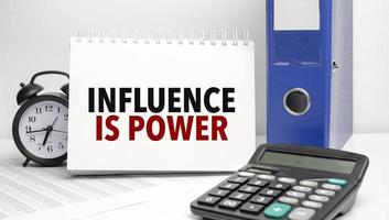 influence is power words on white notebook and calculator, black vintage alarm clock and blue paper folder photo