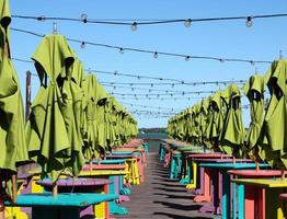 Empty waterside patio with colorfull tables, stools and green umbrellas photo