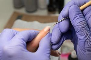 el proceso de creando un francés manicura. manicuro sorteos un blanco raya en el clavo. gel polaco revestimiento foto