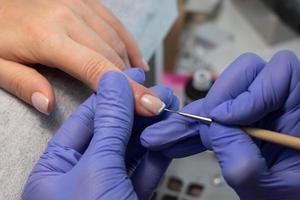 el proceso de creando un francés manicura. manicuro sorteos un blanco raya en el clavo. gel polaco revestimiento foto