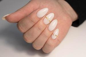 hermosa desnudo manicura con perlas y oro rayas. manicura para mujer con gel polaco. largo uñas en el forma de Almendras foto