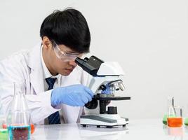 Asian male student scientist Wearing a doctor's gown in the lab looking hand at chemist. caused by mixing reagents in scientific research laboratories with test tubes and microscope on the table photo