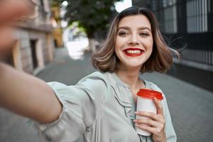 cheerful woman taking a selfie on the street with a cup of coffee photo