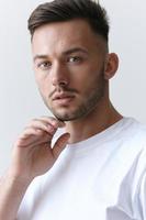 Portrait shot of handsome pensive romantic serious tanned man guy in basic t-shirt looks at camera posing on white background. Fashion Style New Collection Offer. Copy space for ad. Model snap photo