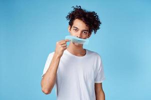 cute man with curly hair holding comb in hand and blue background cropped view photo