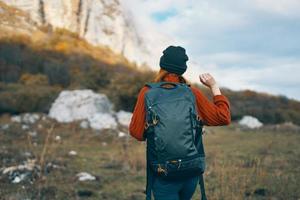 a traveler in a sweater and a hat is resting in the mountains in nature and a backpack on her back photo