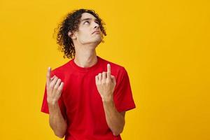 Pensive funny Caucasian young man in red t-shirt point at copy space posing isolated on over yellow studio background. The best offer with free place for advertising. Emotions for everyday concept photo
