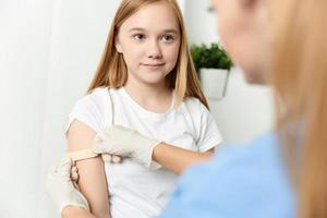 el médico siguiente a el niña pegamentos su mano con un yeso de cerca foto