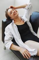 mujer acostado a hogar en el sofá retrato con un corto Corte de pelo en un blanco camisa, sonrisa, depresión en adolescentes, hogar fiesta foto