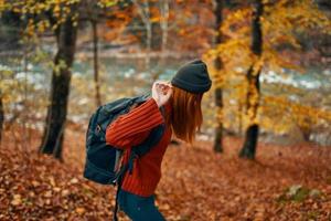 woman hiker with backpack in autumn forest near mountain river and fallen leaves photo