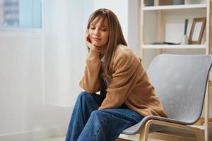 Lovely young blonde lady in warm sweater nostalgic remembers pleasant moments recline on hand sitting in armchair at home. Pause from work, take a break, reflections in free time concept. Copy space photo