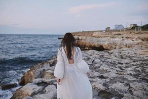 A woman in a white dress walks on the rocks back view unaltered photo
