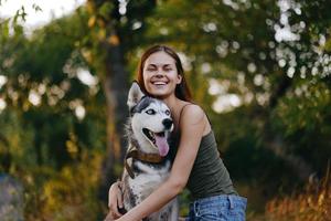 alegre mujer con un fornido raza perro sonriente mientras sentado en naturaleza en un caminar con un perro en un Correa otoño paisaje en el antecedentes foto