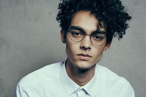 portrait of a nice guy with curly hair on a gray background and a light shirt glasses model close-up photo
