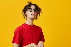 Funny cute myopic young student man in red t-shirt eyewear posing isolated on over yellow studio background. The best offer with free place for advertising. Education College concept photo