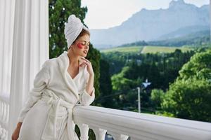 mujer en un bata de baño con un toalla en su cabeza parches en su cara soportes en el balcón Perfecto soleado Mañana foto