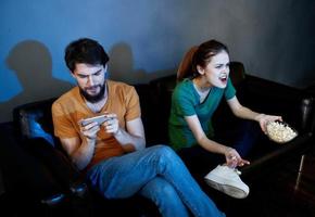 A woman and a man with popcorn on a leather sofa indoors watching TV in the evening photo