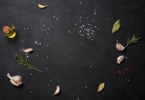 Scattered coarse white salt, peppercorns and rosemary sprigs on a black table, ingredients for cooking fish and meat photo