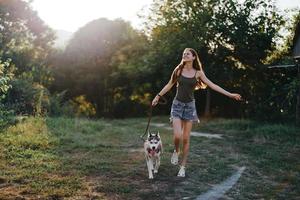 un mujer carreras con un perro en el bosque durante un noche caminar en el bosque a puesta de sol en otoño. estilo de vida Deportes formación con tu amado perro foto