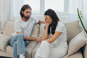 A man and a woman of different races sit on the couch in a room at home and talk about their problems to each other. A stress-free lifestyle of family quarrels with psychological support photo