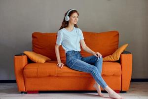 cheerful woman sitting on the couch at home listening to music on headphones technologies photo