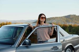 un joven mujer conductor mira fuera de el coche a el otoño paisaje y sonrisas satisfactoriamente foto