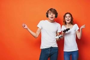 young couple in white t-shirts with joysticks in hands playing game friendship orange background photo