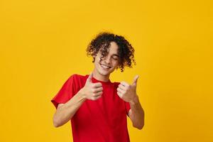 Cheerful funny Caucasian young man in red t-shirt show thumb up gesture posing isolated on over yellow studio background. The best offer with free place for advertising. Emotions for everyday concept photo