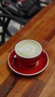 Potrrait green tea latte art in red cup on wooden table in coffee shop photo