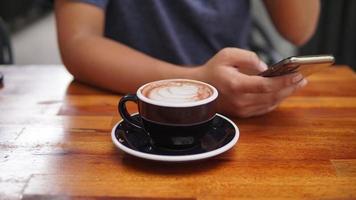Close up image of a cup of coffee and hand using smartphone on wooden table photo