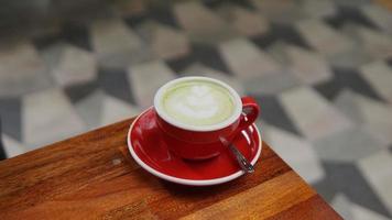 Green tea latte art in red cup on wooden table in coffee shop photo