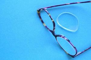 Old broken eyeglasses with damaged lens on blue background. Poor eyesight. Reuse and repair concept. Idea of health. Failure optic eyewear. Breakage of vision correction glasses. Close up, flat lay photo
