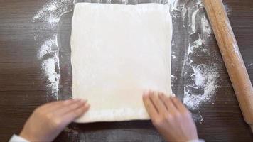 aux femmes mains rouleau en dehors le pâte avec une en bois roulant broche, sur le surface de le tableau. le vue de le Haut video