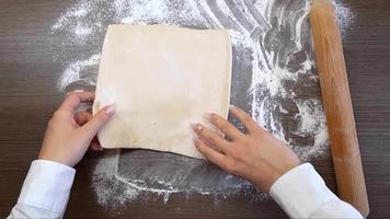 Women's hands roll out the dough with a wooden rolling pin, on the surface of the table. The view from the top video