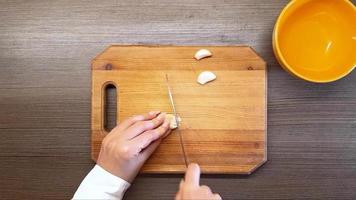 vrouwen handen besnoeiing knoflook met een scherp mes, Aan de oppervlakte van de tafel. de visie van de top video